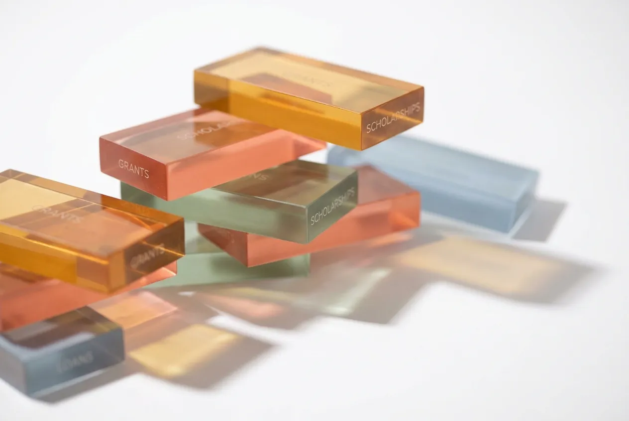 Colored translucent acrylic blocks stacked on a clean white surface, representing layered financial aid sources